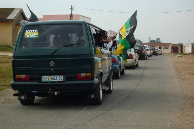 Back of a car with Vote ANC sticker and a person hailing an ANC flag through the window
