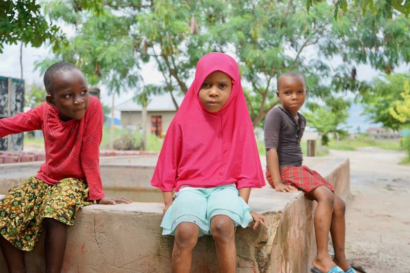 Three kids sitting outside in a village