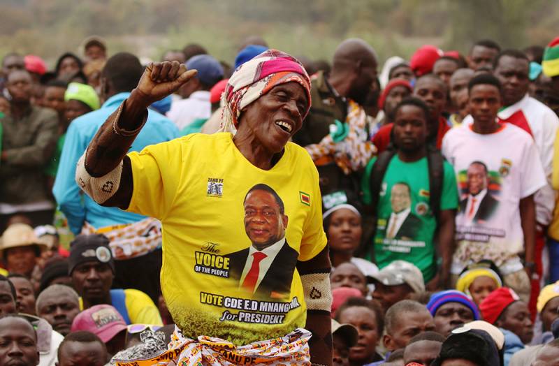 Supporters wait for President Emmerson Mnangagwa to address an election rally of his ruling ZANU (PF) party in Bindura, Zimbabwe. A woman rasing her arm in front