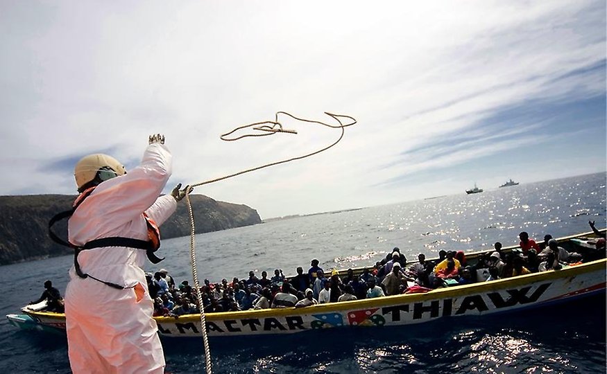 A person from the Spanish coastguard throws a rope to a fishing boat carrying African migrants