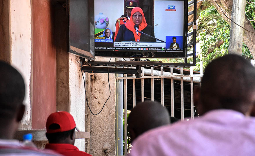 People sitting in a restaurant, with President Suluhu Hassan showing on a wall-mounted TV.