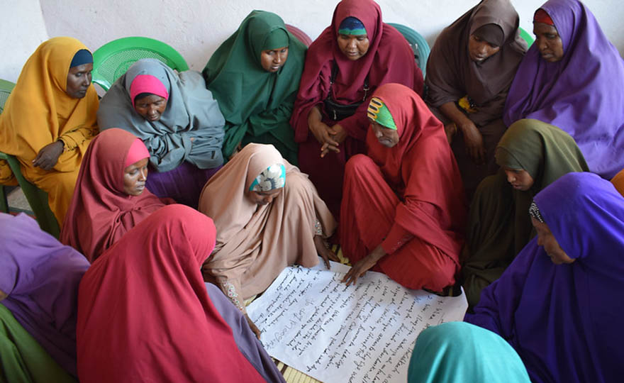 Women from conflicting clans in El Wak, Somalia, sitting inside in a circle with a written document in the middle.