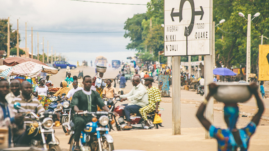 Busiest junction in town with a lot of street sellers, people walking, people on motorcykles and transportation connections. Sign on this junction shows directions to south and north Benin, also to Nigeria and Togo.