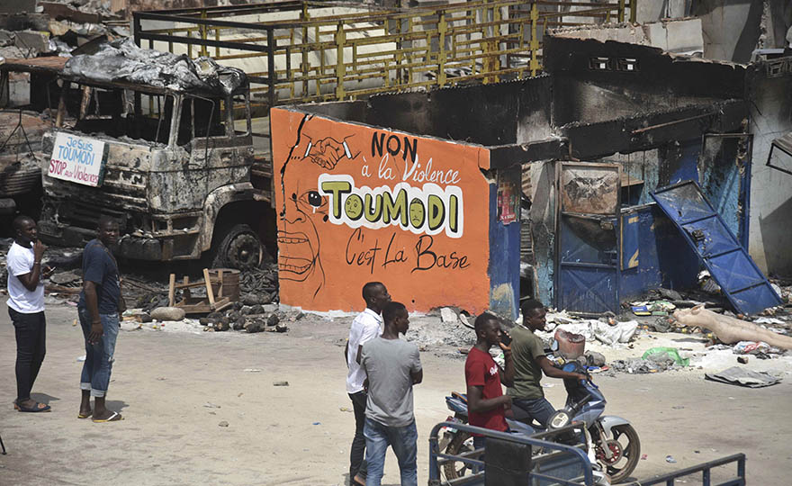 People stand near a wall of a damaged shop that reads: "no to violence, Toumodi is the basis" in the market of Toumodi on November 4, 2020, during a campaign of non-violence and peace awareness by young volunteers after inter-community clashes during the country's presidential election of October 31, 2020