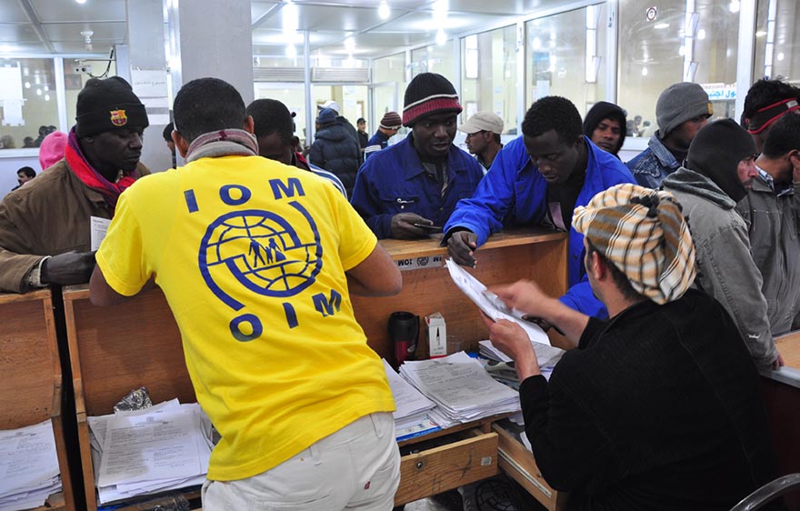 Several migrants getting help with documents at a desk by IOM officials.