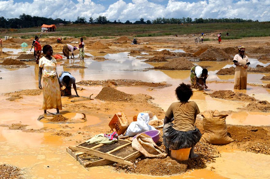 Woman sitting washing copper ore by a river. 