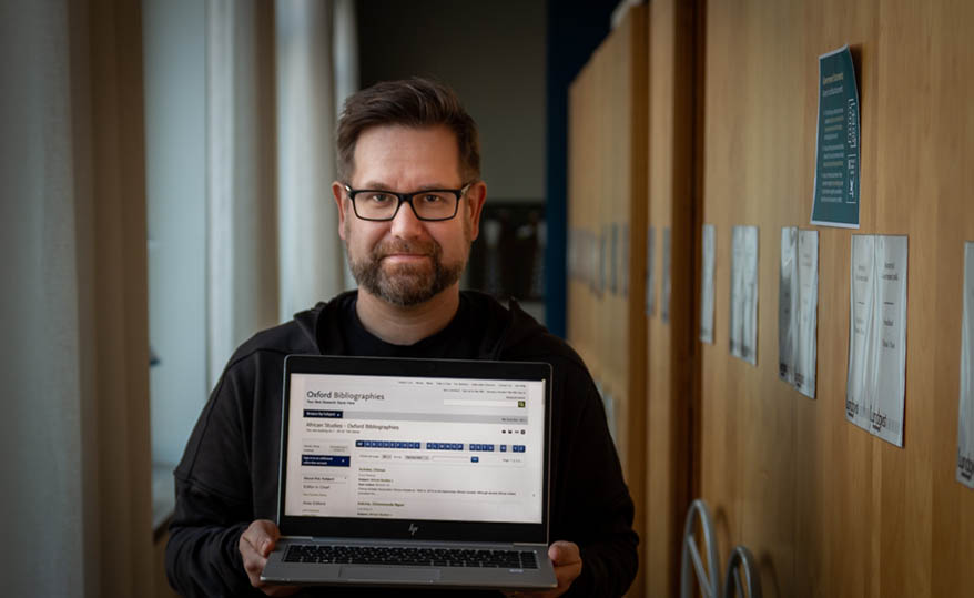 Librarian Kalle Laajala holds up a laptop computer with the Oxford Bibliographies database for academic articles.