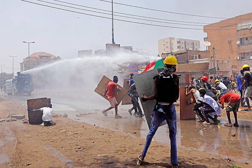 Khartoum, Sudan, 30 June 2022. Protesters take cover as riot police try to disperse them with a water cannon. Photo: AFP.