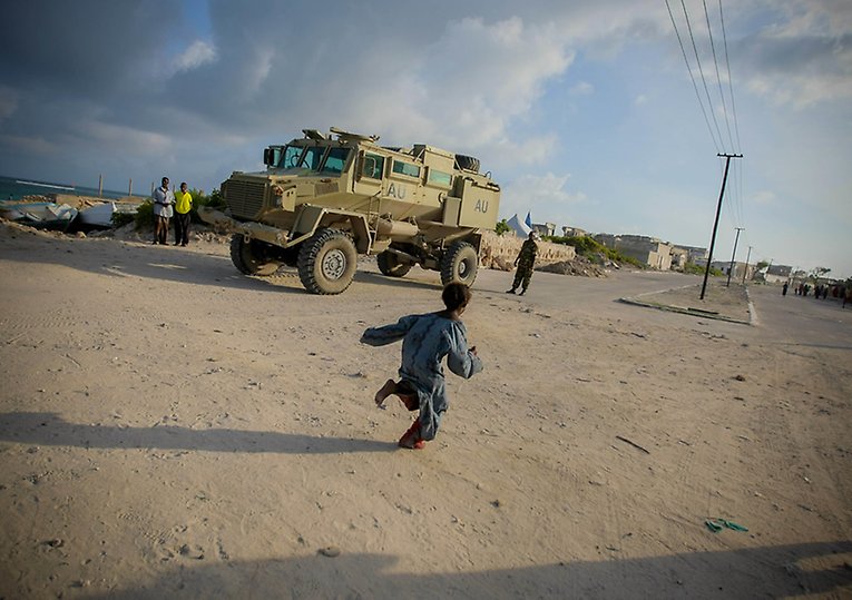A young Somali girl runs in front of an AMISOM armed personnel carrier in Lido Beach in the Kaaraan District of Mogadishu, Somalia.