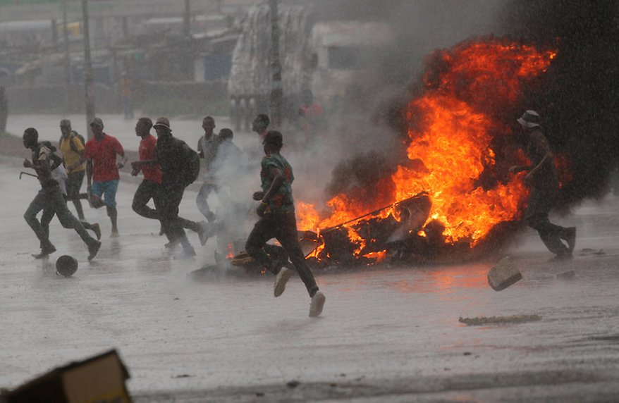 People run at a protest as barricades burn during rainfall in Harare