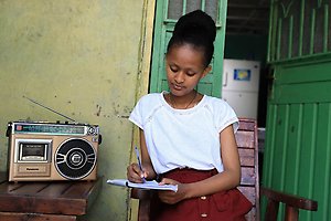 Girl writing at table with a radio
