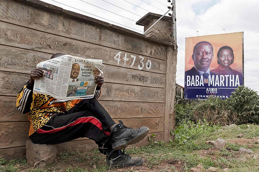 Nairobi, 10 August 2022. A man reads the Daily Nation newspaper while seated near a campaign billboard of Raila Odinga and his running mate Martha Karua, following Kenya's general election. Photo by Tony Karumba, AFP.